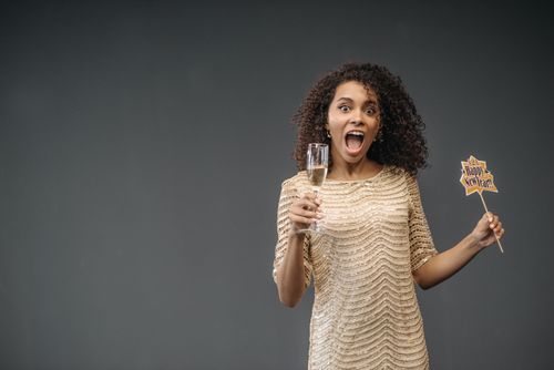 Free Excited woman in elegant dress celebrating New Year's Eve with champagne and a party sign. Stock Photo
