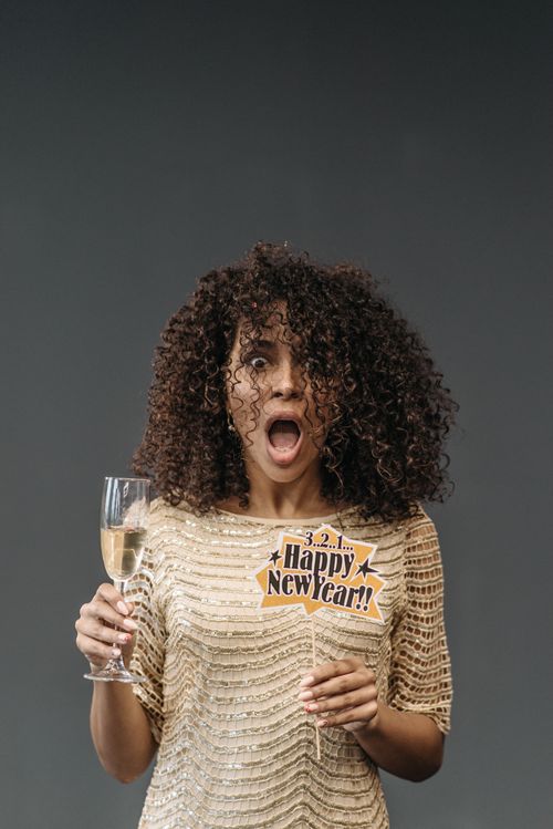Free Astonished woman in a festive dress holding champagne and Happy New Year sign. Stock Photo