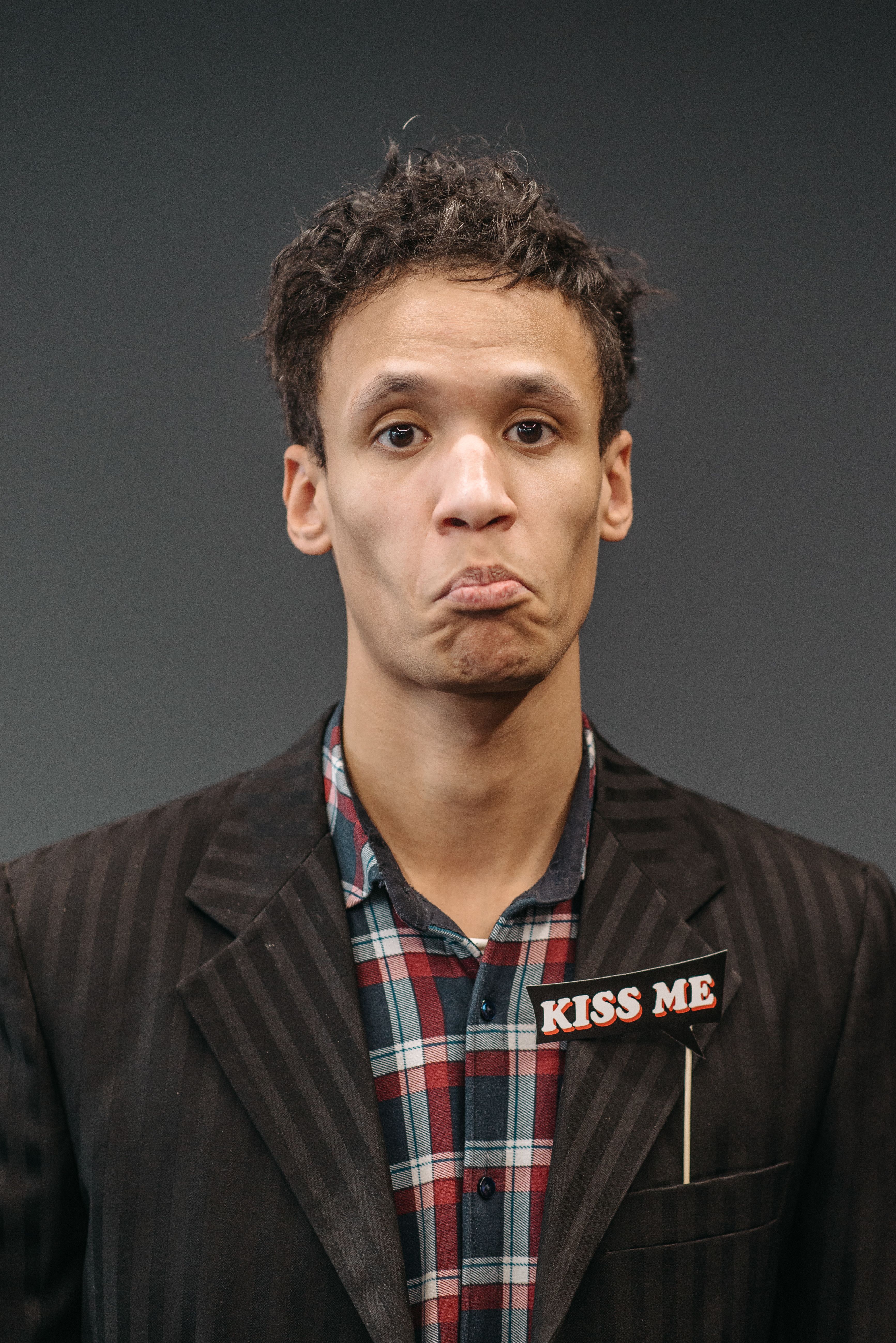 Man in formal attire with a cute pout and 'Kiss Me' badge, expressive portrait.