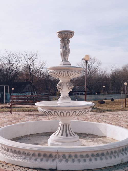 Free A beautifully ornate white marble water fountain in an outdoor setting, ideal for decorative garden themes. Stock Photo