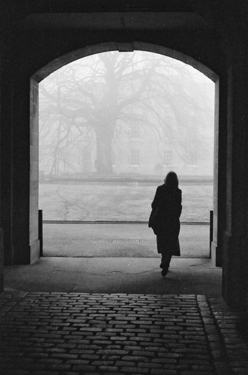 Free A silhouette of a woman walking under an archway into a foggy Oxford street. Stock Photo