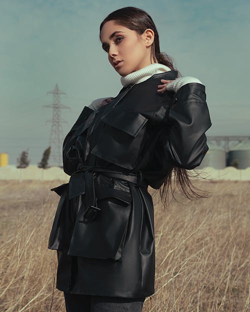 A Woman in Black Leather Coat Standing on Brown Grass Field