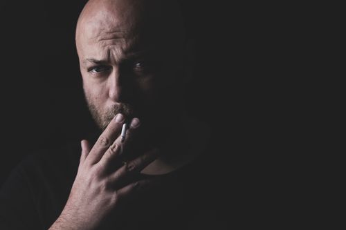 Free Dramatic close-up of a bald man smoking in a dark studio setting, highlighting facial emotion. Stock Photo