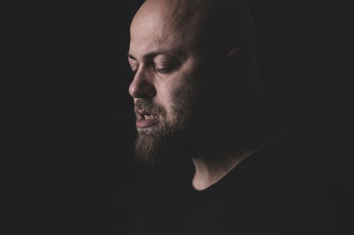 Free Close-up moody portrait of a bearded bald man in a dark studio setting. Stock Photo