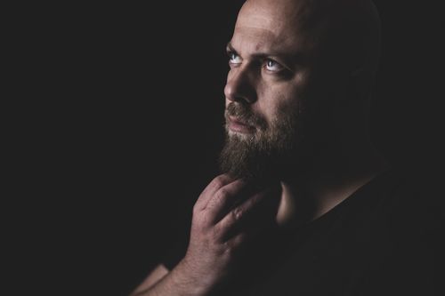Free A close-up portrait of a bald man with a beard, looking contemplatively upwards in a studio setting. Stock Photo