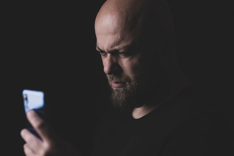 A man examining his phone closely with a skeptical expression in low light