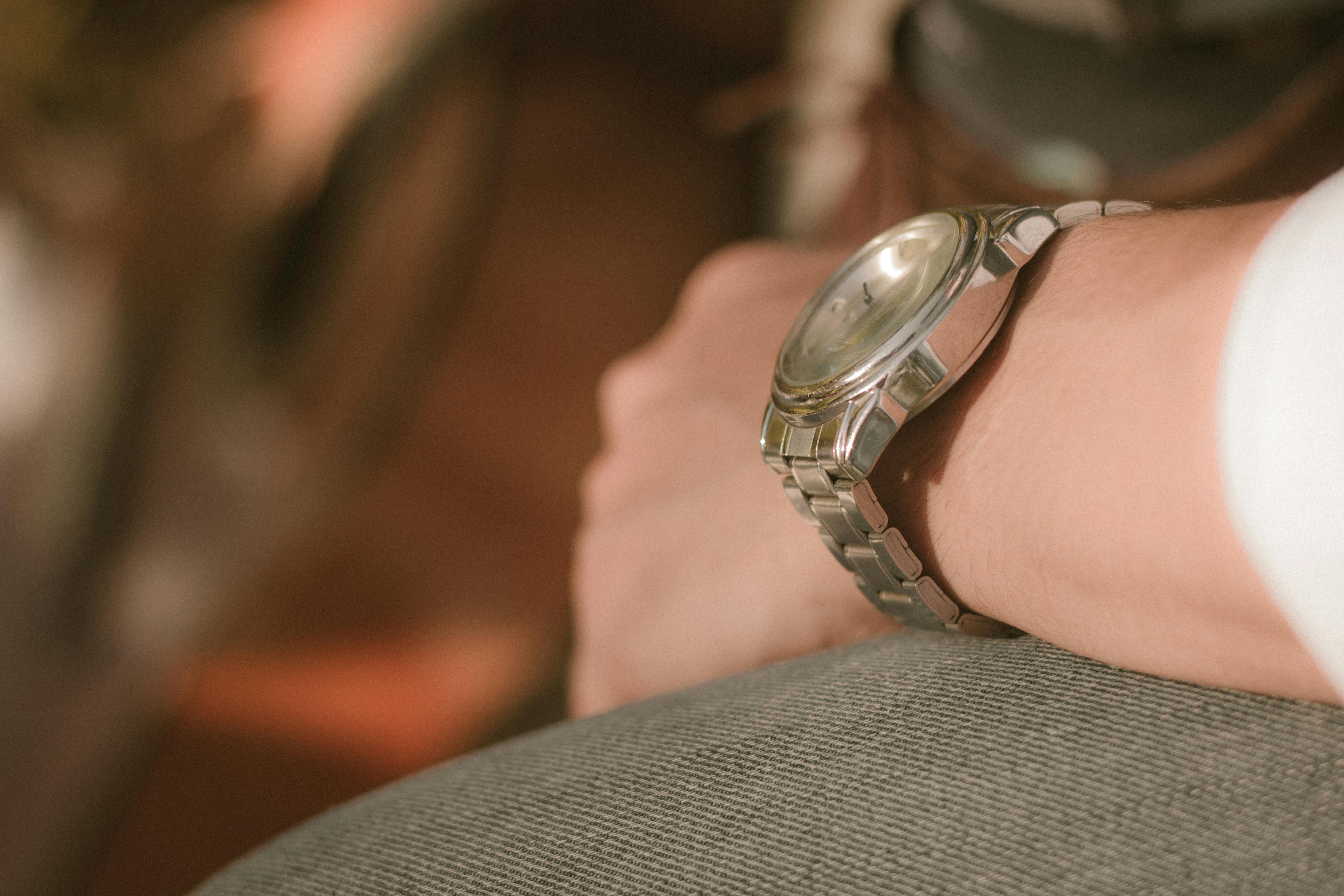A silver wristwatch worn by a man resting on a textured cushion in a warm outdoor setting.