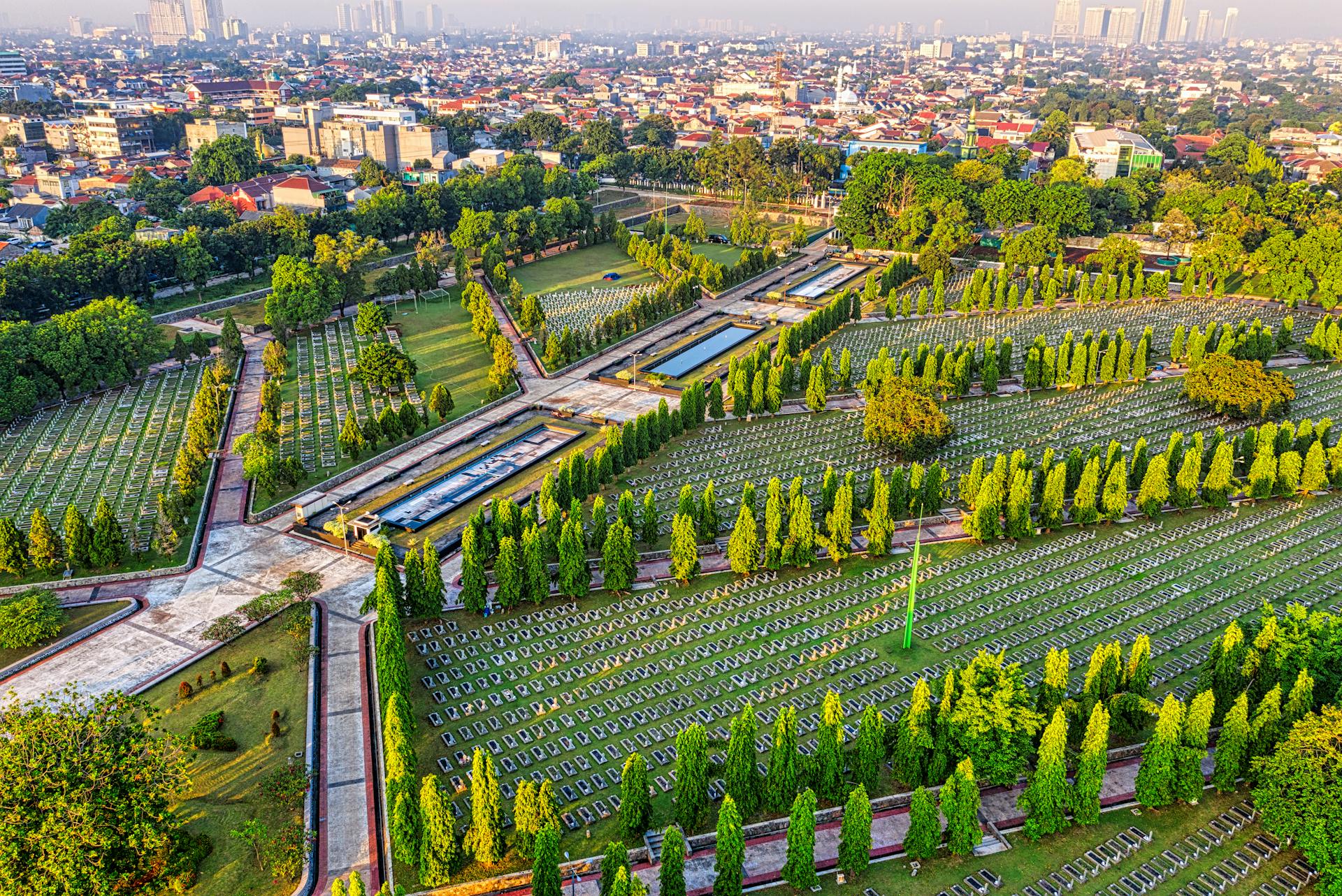 Drone view of main heroes cemetery with gravestones and alley surrounded by green trees located in Kalibata city with residential buildings