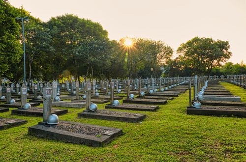 Free Tombstones with military helmets located on grassy ground in national heroes cemetery with lush green trees in Kalibata in Indonesia Stock Photo