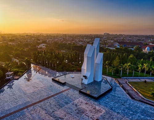 Drone view of contemporary building located on paved square in national main heroes cemetery among green trees in Indonesia at sunset time