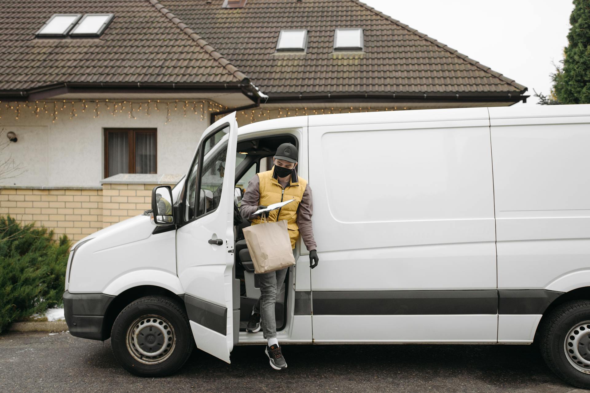 Delivery person carrying a package from a white van outside a house, showcasing efficient home delivery service.