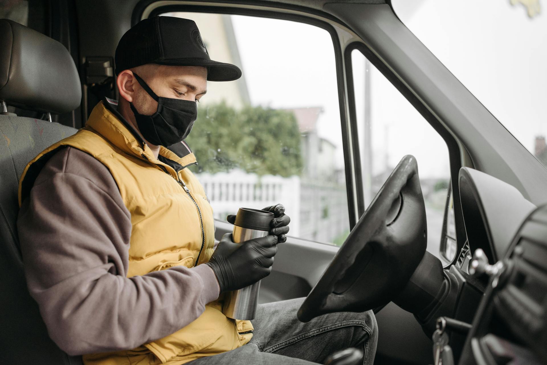 Delivery driver holding a thermos and wearing a facemask in a van.