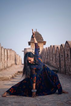 A woman doing a yoga pose outdoors in a colorful maxi dress on a historic walkway.