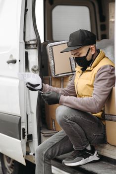 A courier wearing a face mask and gloves reading a document inside a delivery van.