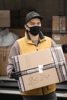 A delivery man carrying a package outdoors, wearing a face mask and gloves for safety.