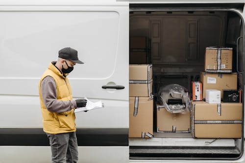 Man Wearing Face Mask Standing Near Vehicle Door with Brown Carton Boxes