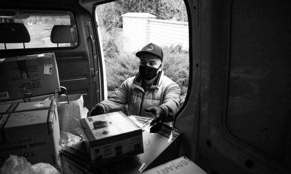 Delivery Services โ A deliveryman in a van organizing boxes, masked for safety, in a grayscale image.