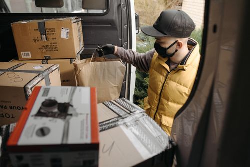 Free A masked deliveryman loads packages into a van, illustrating modern logistics. Stock Photo