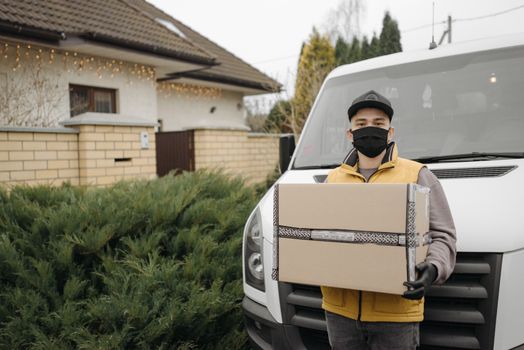 Courier wearing a mask delivering a package outdoors in front of a van.