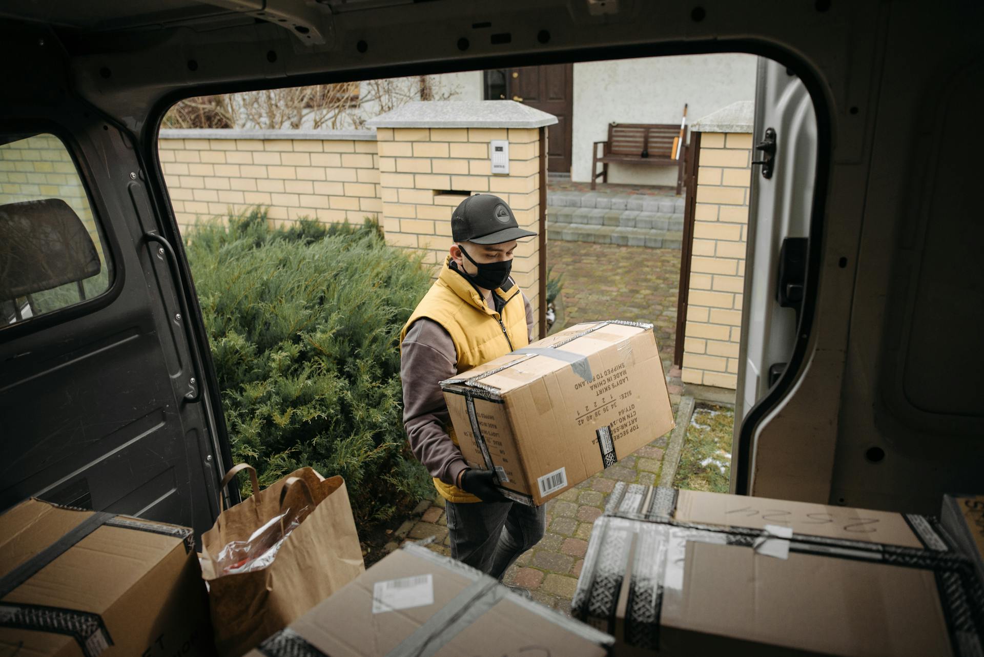 Masked courier unloading packages from a delivery van in a residential area.