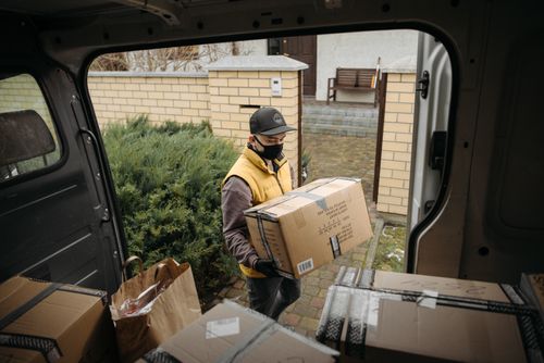 Free Masked courier unloading packages from a delivery van in a residential area. Stock Photo
