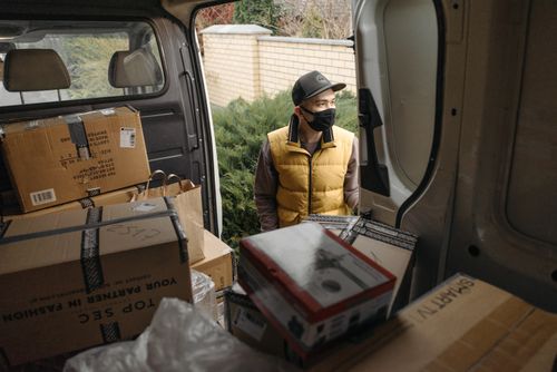 Free Courier in a mask loading packages into a van. Safe, modern logistics during new normal. Stock Photo