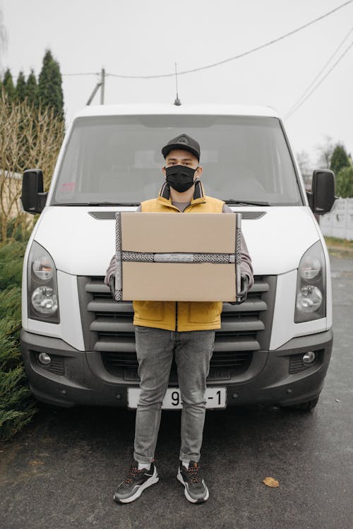 Free Man with a Box Standing Beside a Delivery Van Stock Photo
