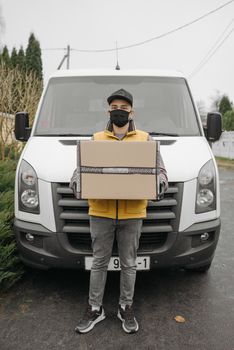Delivery man with mask carrying package in front of a delivery van during the pandemic.