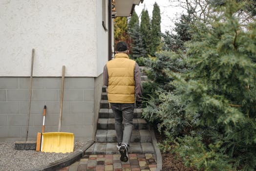 A man in a yellow vest walks towards a house surrounded by greenery.