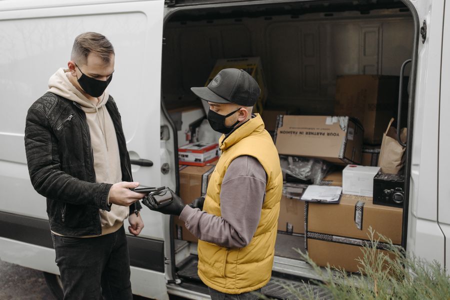 Courier handing over package to customer for contactless delivery by a van.