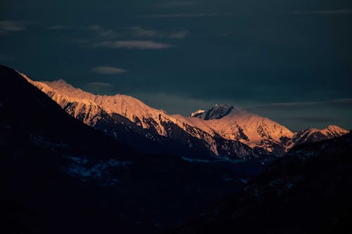 Rocky mountains with snowy peaks under blue sundown sky