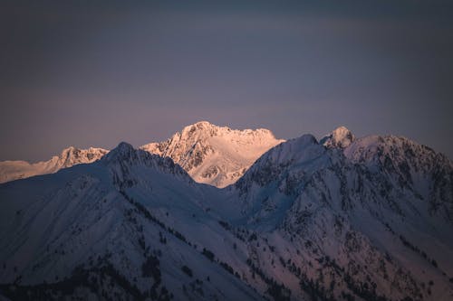Picturesque rocky mountain range covered with snow against cloudless sunset sky in winter