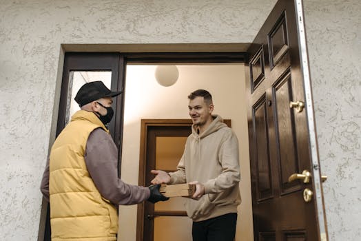 A deliveryman with a facemask delivers a package to a man at the door.