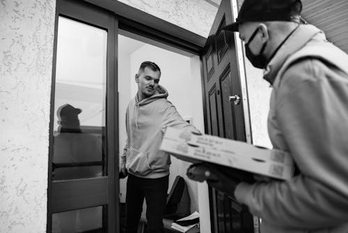 Grayscale Photo of a Man Delivering Pizza to Another Man
