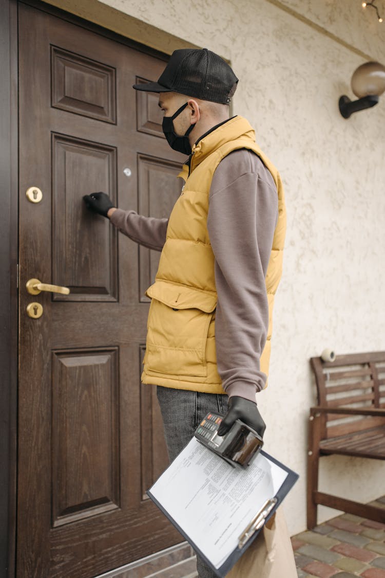 Man Holding Credit Card Terminal And Paper Knocking On Door