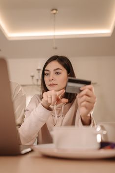 Woman holding credit card shopping online on laptop indoors.
