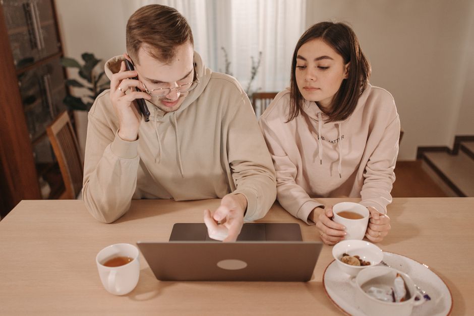 A couple enjoying coffee and online shopping together at home, using a laptop and smartphone.