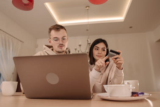 A young couple using a laptop and credit card for online shopping in a cozy indoor setting.