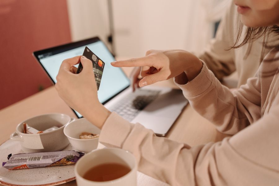 A woman using a credit card for online shopping while having tea and snacks on a table.