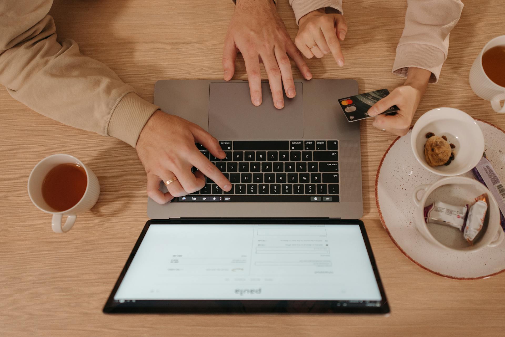 Two people using a laptop for online shopping with a credit card, seen from above.