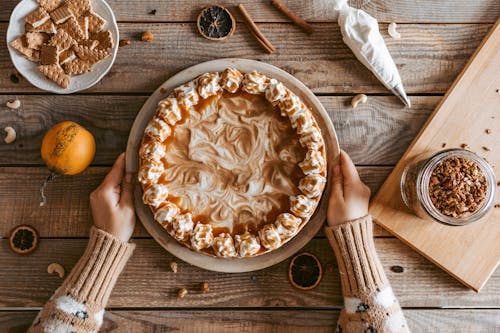 Top view crop anonymous female in sweater serving freshly baked yummy pie with whipped cream on wooden table