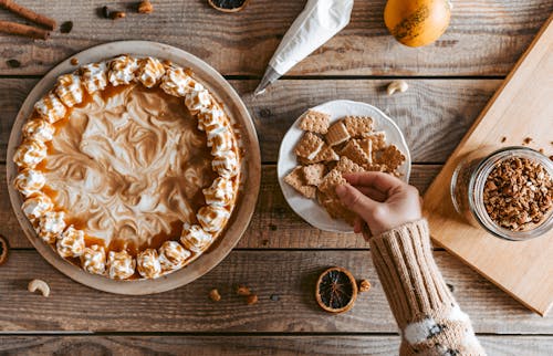 Crop unrecognizable woman taking cookie served on table near pie