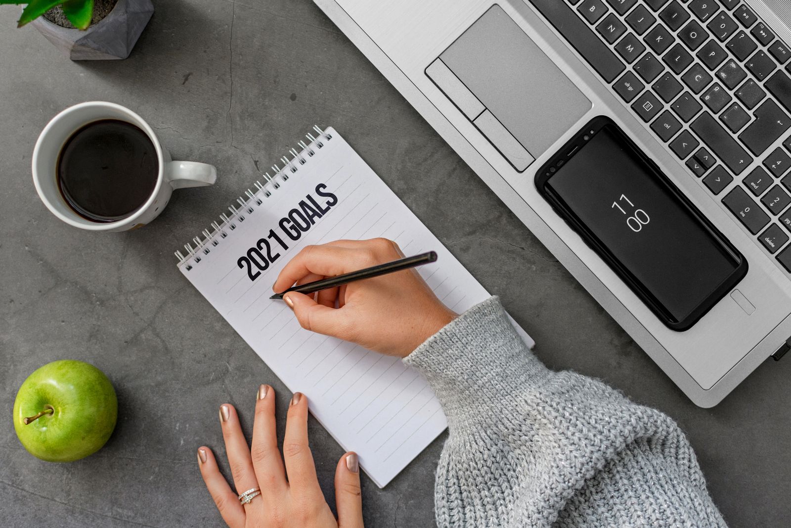 Person writing goals in a notebook beside a laptop