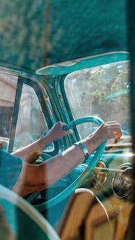 A driver navigates an old vintage car, hands on the steering wheel, sunlight streaming through the window.