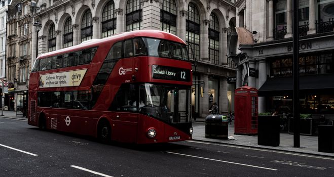 A classic red double-decker bus on a historic London street, showcasing urban life in the UK.