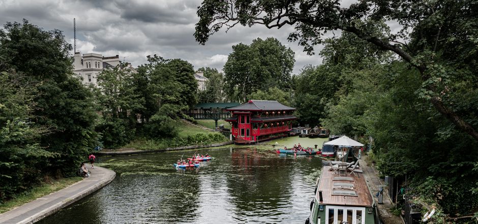 Picturesque canal scene with kayakers, a red building, and lush greenery in London.