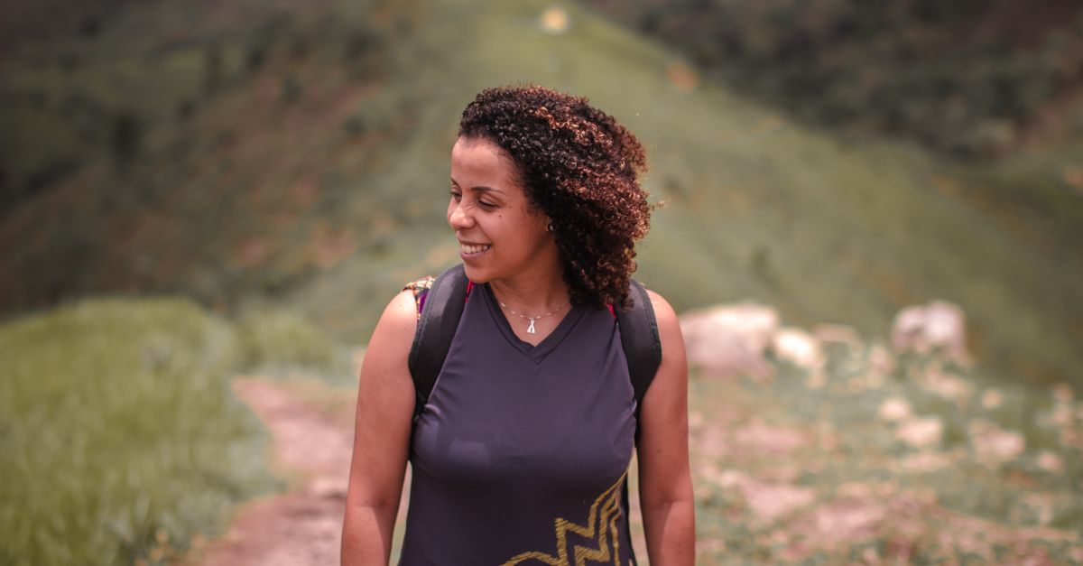 A person smiling while hiking on a mountain trail, away from a city in the background