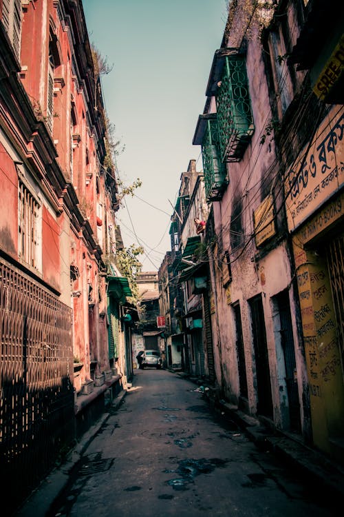 Shabby buildings with narrow paved street located in old poor district of city on day with good weather