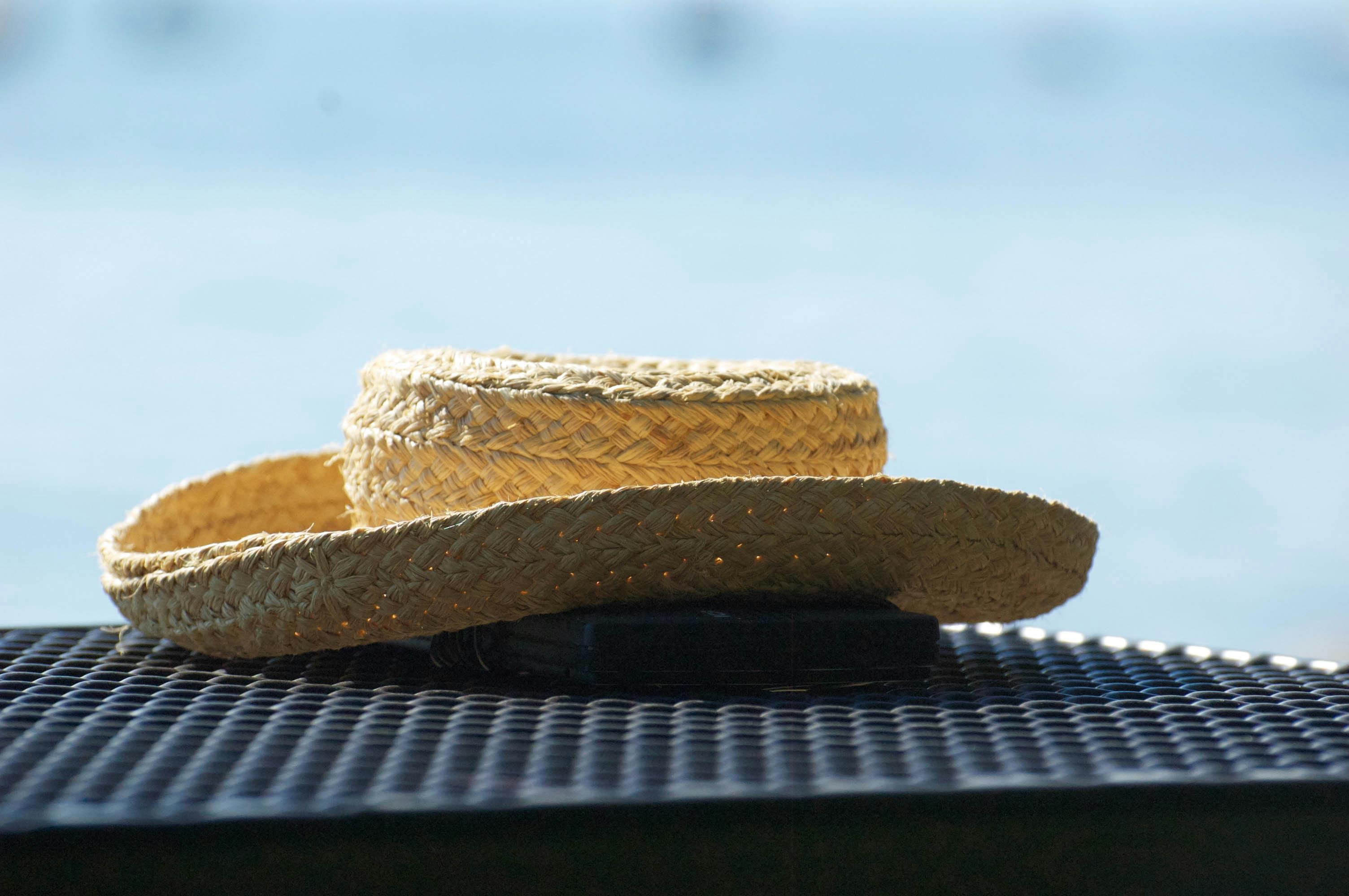 Close-up of a woven straw hat on a black table, sunlight on a blurred water background.