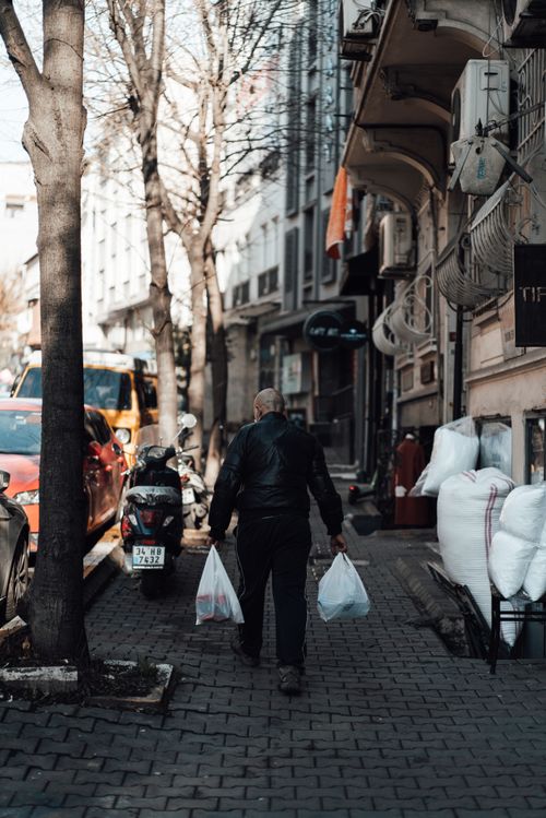 Free Full body back view of anonymous male pedestrian carrying shopping packets walking on pavement near old buildings Stock Photo